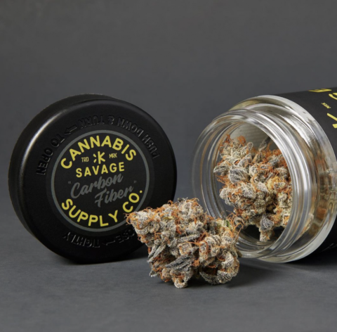 High-quality CBD flower bud shown with its original packaging, featuring a black 'Savage Carbon Fiber' lid and glass jar